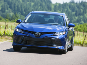 a blue 2020 Toyota camry driving on a road in front of trees and hills