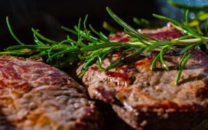 a cooking steak with a sprig of rosemary on top